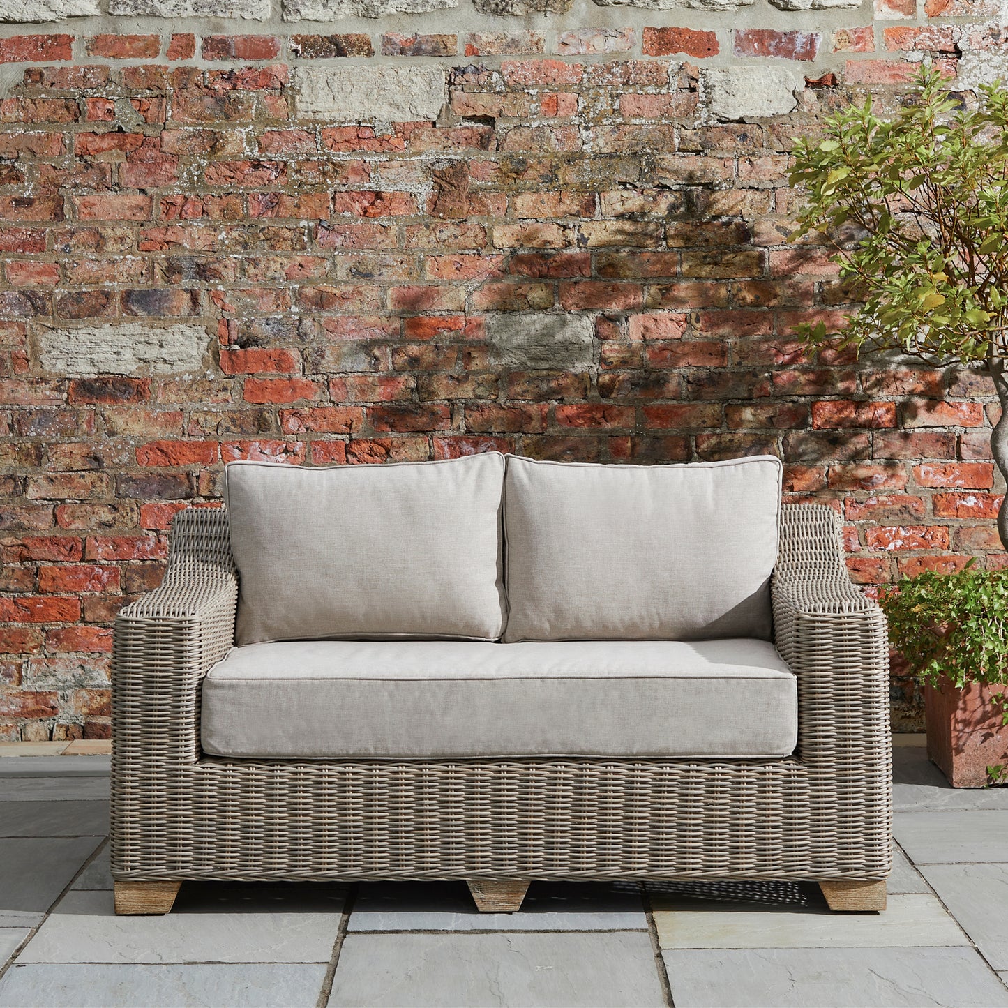Hill Interiors Capri Collection beige outdoor two seater sofa in a modern garden setting