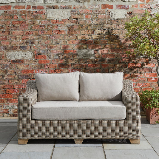 Hill Interiors Capri Collection beige outdoor two seater sofa in a modern garden setting