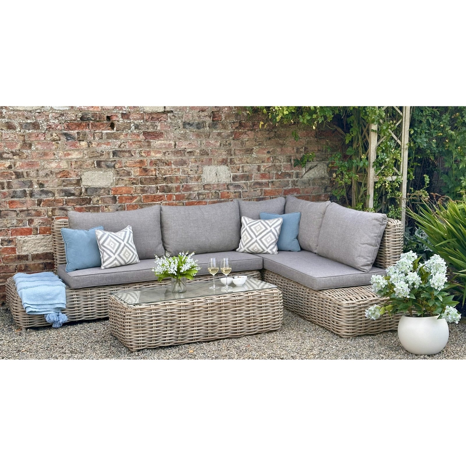 Hill Interiors Amalfi Collection beige outdoor large corner set with glass table in a modern garden setting