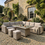 	Hill Interiors Amalfi large outdoor corner set with riser table and 2 stools in beige fabric in a modern garden setting