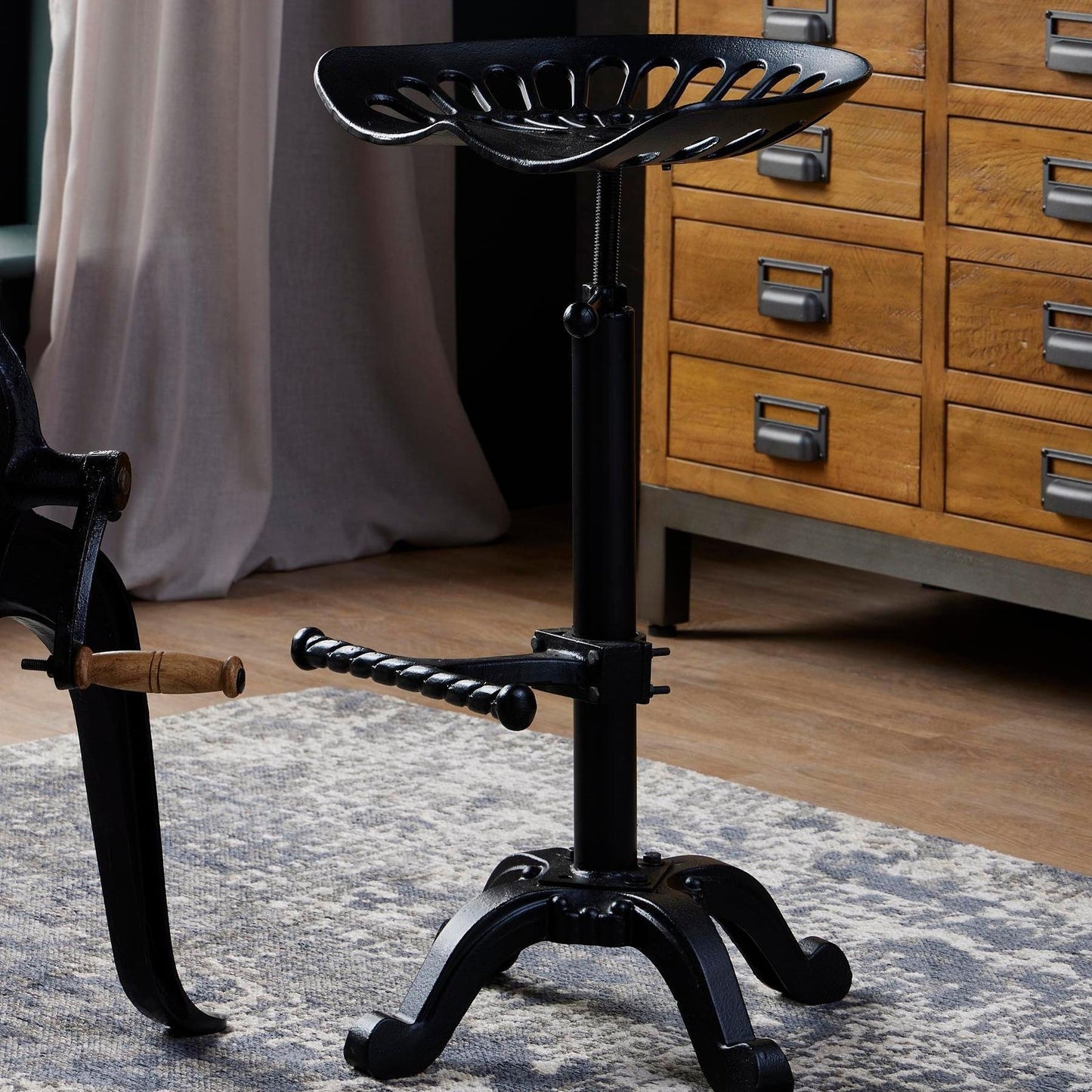	Hill Interiors adjustable tractor seat stool with black metal frame and shaped seat, placed in an industrial kitchen setting