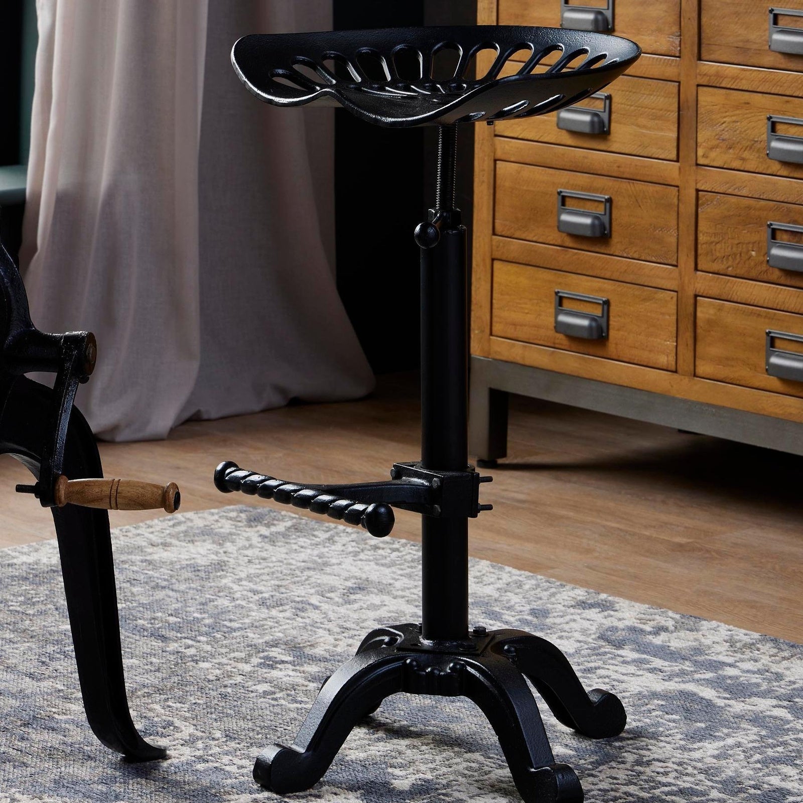 	Hill Interiors adjustable tractor seat stool with black metal frame and shaped seat, placed in an industrial kitchen setting